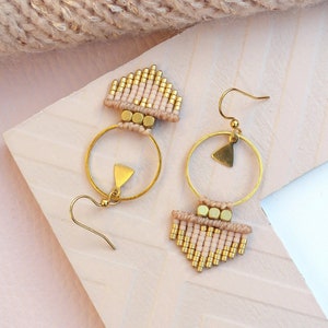 May include: A pair of gold hoop earrings with a pink and gold beaded fringe. The earrings have a triangular charm hanging from the hoop.