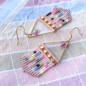 Peut inclure: Boucles d'oreilles faites à la main avec un design géométrique. Les boucles d'oreilles présentent une frange de perles roses, des accents en métal doré et des perles colorées. Chaque boucle d'oreille a un crochet doré et un petit cristal irisé.