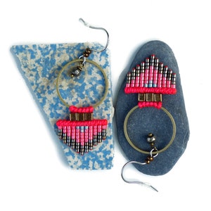 Könnte beinhalten: Ein Paar Ohrringe aus rosa und silbernen Perlen mit geometrischem Muster. Die Ohrringe hängen an einem grauen Stein.