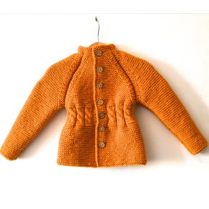 May include: A mustard yellow long-sleeved knit cardigan featuring a high collar, a vertical row of six small brown buttons down the center front, and a textured cable knit detail cinched at the waistline, displayed on a wire hanger.