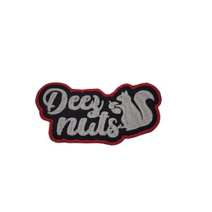 May include: A black and white embroidered patch with red stitching. The patch features the text "Deez Nuts" with a squirrel holding a nut.