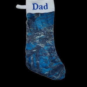 Puede incluir: Calcetín de Navidad de camuflaje azul y blanco con un puño blanco y la palabra "Papá" bordada en azul.