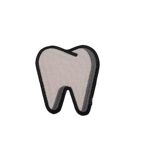 Puede incluir: Un parche blanco en forma de diente con un contorno negro. El parche está hecho de un material suave y peludo.