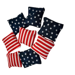 May include: Eight bean bags in a circle, four are red and white striped and four are blue with white stars. The bean bags are made of fabric and are designed to look like the American flag.