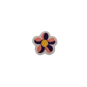 May include: A pink and purple flower patch with a yellow center. The flower is embroidered on a white fabric.