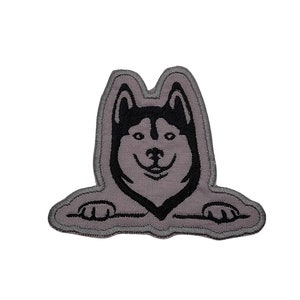 May include: A gray embroidered patch of a black and white husky dog peeking over a gray border.