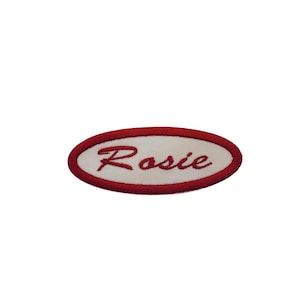 May include: White oval-shaped embroidered patch with a red border. The name "Rosie" is embroidered in red cursive lettering.