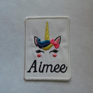 May include: White embroidered patch featuring a unicorn design and the name "Aimee" in black cursive lettering.