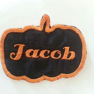 May include: An orange and black pumpkin-shaped patch with the name "Jacob" embroidered in orange thread.