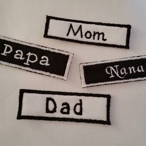 May include: Four black and white embroidered patches with the words "Mom", "Papa", "Nana", and "Dad" in white lettering.