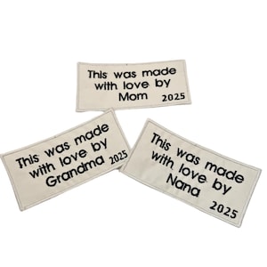 May include: Three white fabric labels with black text. The labels say "This was made with love by Mom 2025", "This was made with love by Grandma 2025", and "This was made with love by Nana 2025".