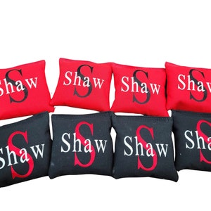 May include: Eight bean bags with the name "Shaw" embroidered on them. Four bean bags are red with white lettering and four bean bags are black with red lettering.