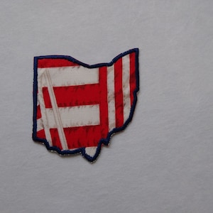 May include: A red, white, and blue fabric patch in the shape of the state of Ohio. The patch is outlined in navy blue.