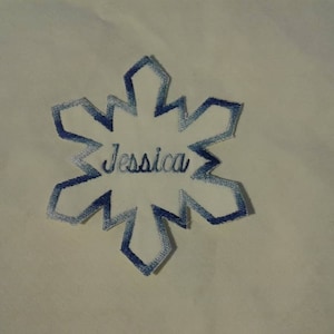 Puede incluir: Un parche en forma de copo de nieve azul y blanco con el nombre "Jessica" bordado en el centro.