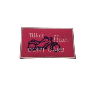 May include: Pink embroidered patch with white text that reads "Biker Hair Don't Care" and a black motorcycle graphic.