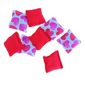 May include: A set of eight bean bags in red and white with a heart pattern. The bean bags are made of fabric and are filled with beans. They are perfect for playing games or for decoration.
