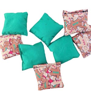 May include: Eight bean bags for a game. Four bean bags are green and four bean bags are brown with a gingerbread man pattern.
