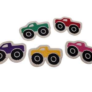 Puede incluir: Cinco parches de camión monstruo en diferentes colores: verde, rojo, morado, amarillo y rosa. Cada parche tiene ruedas negras y un contorno blanco.