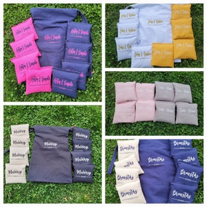 May include: A selection of personalised cornhole game sets and bags in shades of pink, navy, white, and gold. Each set is customised with names and dates, ideal for events and celebrations.