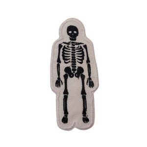 May include: White fabric patch with a black embroidered skeleton design. The skeleton is standing with its arms at its sides.