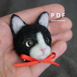 以下が含まれることがあります： 赤いリボンをつけた黒と白のフェルトの猫の頭。猫は胸に白い斑点があり、鼻はピンク色です。猫は手で持たれています。PDF 即時ダウンロード
