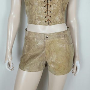 May include: A beige snakeskin-patterned two-piece set consisting of a cropped vest with a front lace-up closure and matching shorts. The shorts feature a standard waistband with a single button closure, belt loops, and two front pockets.