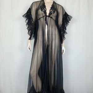 May include: A floor-length black sheer robe featuring delicate lace detailing along the neckline and sleeves. The garment includes wide ruffled sleeves, a tie-front closure, and a ruffled hemline, crafted from a lightweight, translucent fabric.
