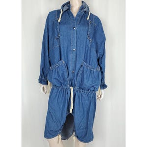 May include: A long, blue denim dress with a hood, long sleeves, and large pockets. The dress features a drawstring waist and hem, and is buttoned down the front. The sleeves have ruffled cuffs. The dress is displayed on a mannequin.