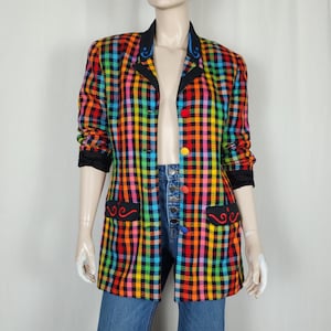May include: A long-sleeved blazer featuring a vibrant multi-coloured plaid pattern in orange, yellow, green, blue, and pink. The garment includes a black collar with blue embroidery, black pocket flaps with red embroidery, and four colourful round buttons.