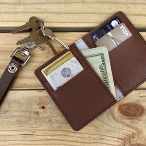 May include: A brown leather wallet with a key chain attached. The wallet is open and has a credit card, cash, and a key in it.