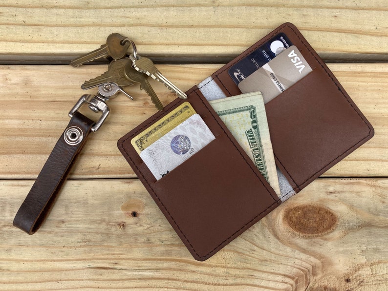 May include: A brown leather wallet with a key chain attached. The wallet is open and has a credit card, cash, and a key in it.