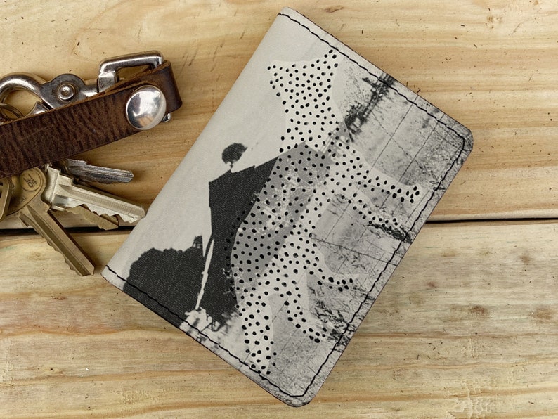 May include: A gray and white leather card holder with a cheetah print design. The card holder has a stitched edge and a subtle distressed look.