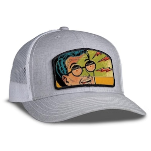 May include: Gray trucker hat with a white mesh back and a curved brim. The front features a rectangular patch with a retro comic book style illustration of a man with the word "STONED" on his glasses. The hat is a classic accessory.