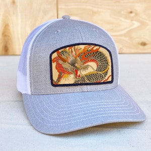 May include: A gray and white trucker hat with a black and white embroidered patch of a red and yellow dragon.