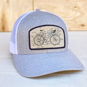 May include: Gray and white trucker hat with a patch featuring a labeled diagram of a bicycle.