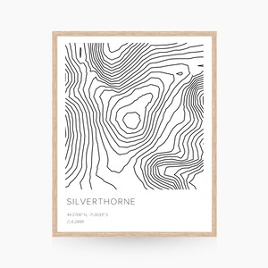 Pode incluir: Uma impressão de mapa topográfico em preto e branco de Silverthorne, Colorado. A impressão mostra as curvas de nível da altitude da área. O texto "SILVERTHORNE", "44.2706° N, 71.3033° S", e "△ 6,289ft" está incluído na impressão.