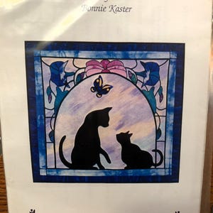 May include: A quilt pattern titled "The Cats Meow" by Bonnie Kaster. The pattern features two black cats, a butterfly, and a stained glass style design with blue, purple, and pink colors. The text "Sweet Memories" is at the bottom of the pattern.