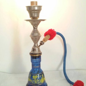 May include: A blue glass hookah with a silver base and a red and blue hose. The hookah has a decorative design with palm trees and other motifs.