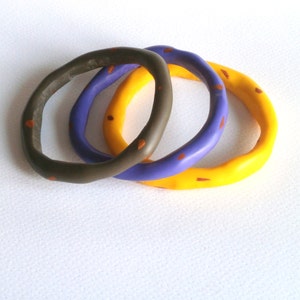 Op de afbeelding: Drie kleurrijke armbanden met een gespikkeld patroon. De armbanden zijn geel, paars en donkergroen.