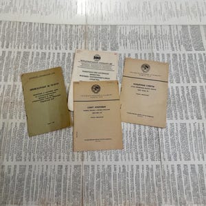 Op de afbeelding: Een verzameling vintage documenten met verbleekte bruine covers en Cyrillische tekst. De documenten liggen op een krantenachtergrond. Titels zijn onder meer "Preskourant", "Mezhdunarodny Standart" en "Konye Spirty".