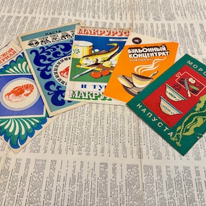 Op de afbeelding: Een verzameling vintage voedselverpakkingen, met kleurrijke ontwerpen en Cyrillische tekst. De verpakkingen bevatten illustraties van zeevruchten, kommen en andere voedingsmiddelen. De items zijn gerangschikt op een krantenachtergrond.