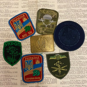 May include: A collection of embroidered patches featuring the Ukrainian coat of arms and various military insignia. The patches are in different colours, including blue, yellow, green, and red. The patches are arranged on a page with text in Ukrainian.