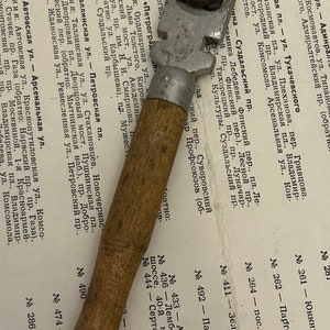 May include: A close-up of a silver and wooden glass cutter. The cutter has a wooden handle and a silver blade with a small wheel. The cutter is resting on a page of a book with a list of street names and numbers.