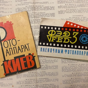 May include: Two vintage camera instruction manuals. The first manual is for a "Kiev" camera and features a red and black illustration of a camera with the text "OTO-APPARAT" above it. The second manual is for a "FED" camera and features a yellow and black illustration of a camera with the text "ПЛЕНОЧНЫЙ ФОТОАППАРАТ" below it.