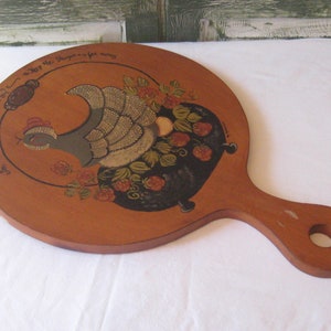 May include: A wooden cutting board with a painted design of a hen with a pot of berries. The text "For Eggs & Inspiration, may the Kitchen be for always" is painted around the edge of the board.
