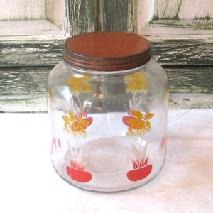 May include: A clear glass jar with a red metal lid. The jar has a floral design with yellow and red flowers.