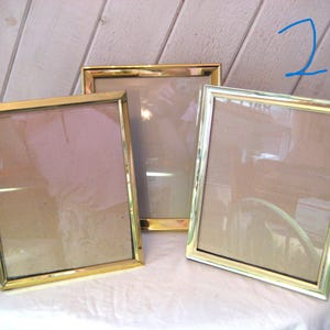 Puede incluir: Tres marcos de fotos rectangulares con bordes de metal dorado. Los marcos est&aacute;n vac&iacute;os, con vidrio o pl&aacute;stico transparente que cubre las aberturas. Los marcos est&aacute;n colocados sobre una superficie blanca.
