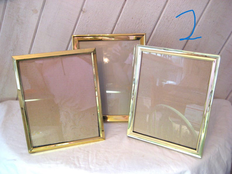 Puede incluir: Tres marcos de fotos rectangulares con bordes de metal dorado. Los marcos est&aacute;n vac&iacute;os, con vidrio o pl&aacute;stico transparente que cubre las aberturas. Los marcos est&aacute;n colocados sobre una superficie blanca.