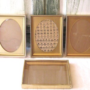 May include: Four vintage gold-toned picture frames. Three frames have oval openings, and one has a rectangular opening. One frame contains a print with hat illustrations and text. The frames are arranged on a white surface.