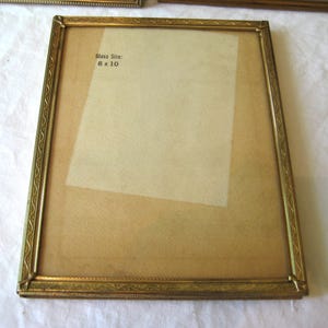 Puede incluir: Un marco de fotos rectangular dorado con un borde ornamentado. El marco tiene un tama&ntilde;o de vidrio de 8 x 10 pulgadas (20 x 25 cm). El marco est&aacute; vac&iacute;o, con un respaldo de color claro visible a trav&eacute;s del vidrio.